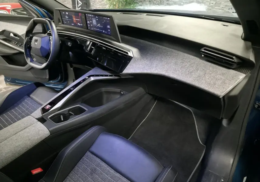 Intérieur avant droit du Peugeot 5008 bleu 2025, tableau de bord avec double écran HD et habillage tissu gris.