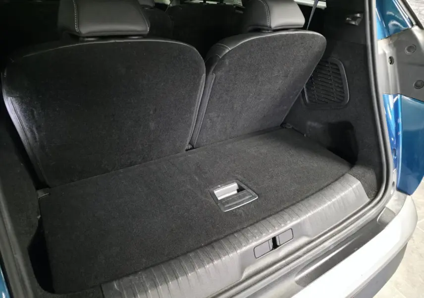 Coffre arrière ouvert d’un Peugeot 5008 bleu, montrant la banquette rabattable et le revêtement noir du coffre.