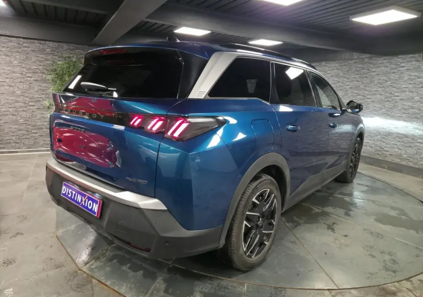 Vue 3/4 arrière droit d’un Peugeot 5008 bleu métallisé avec feux arrière à LED en forme de griffes et jantes alliage noires.