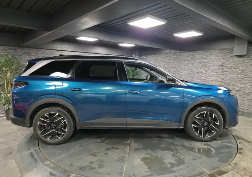 Profil droit d’un Peugeot 5008 bleu métallisé 2025 en intérieur avec jantes alliage noires et toit noir.