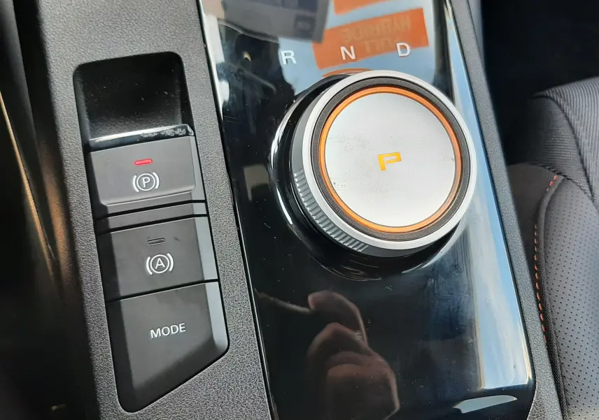 Gros plan sur la molette de sélection de la boîte auto et les boutons de mode et frein à main du MG3 gris intérieur tissu noir.