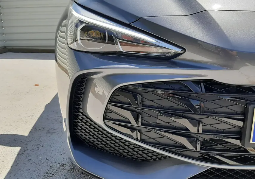Gros plan sur l'avant droit de la MG3 1.5L HYBRID+ 195CH Luxury en gris Hampstead, mettant en valeur le phare et la calandre.