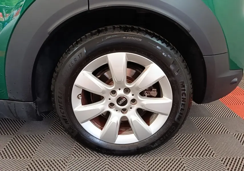 Gros plan sur la roue avant droite d'une MINI Countryman hybride, jante argentée et carrosserie verte visible.