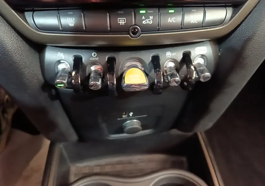 Gros plan sur les commandes centrales avec bouton start/stop jaune dans l’habitacle du MINI Countryman gris clair.