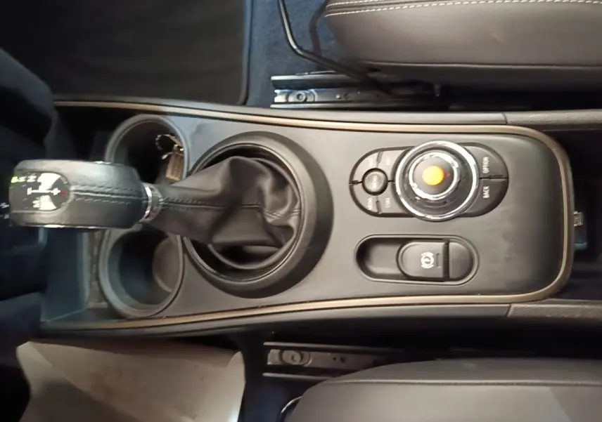 Vue plongeante sur la console centrale noire du MINI Countryman gris clair, avec levier de vitesses et molette de commande.