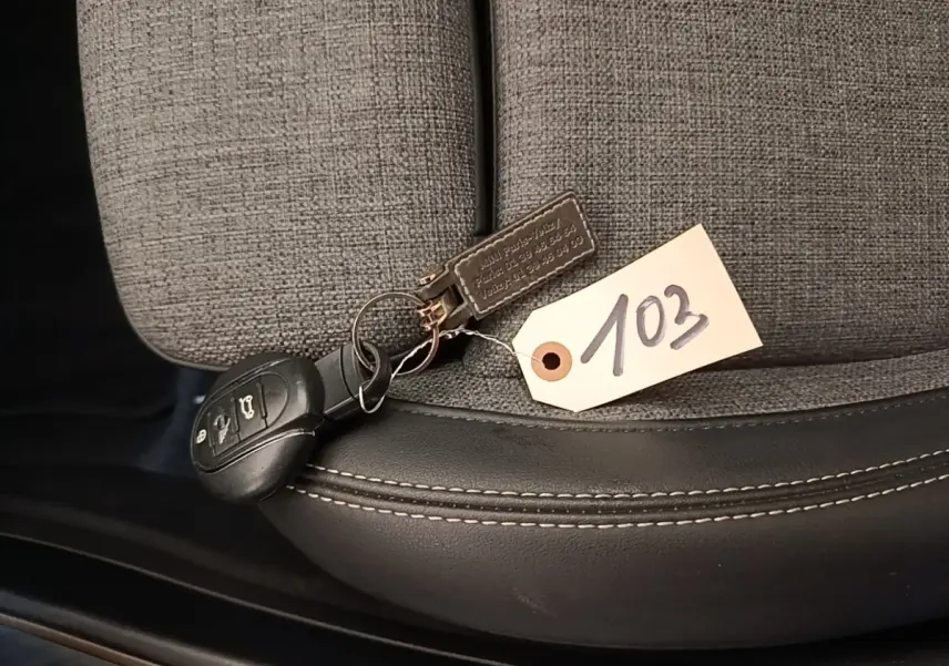 Clé de voiture MINI posée sur un siège tissu gris clair avec bordure cuir noir et étiquette numérotée 103.
