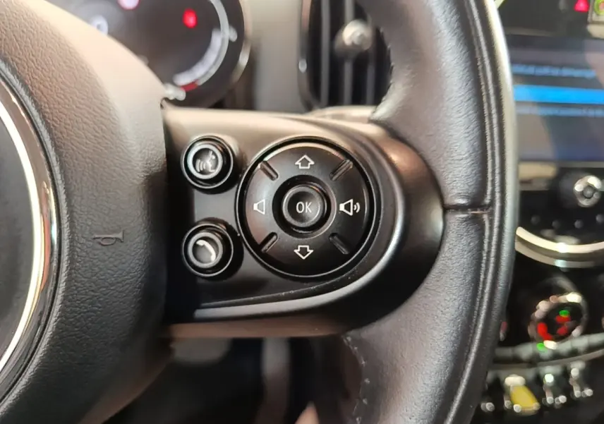 Gros plan sur les commandes multifonctions du volant cuir noir d’un MINI Countryman gris clair, tableau de bord en arrière-plan.