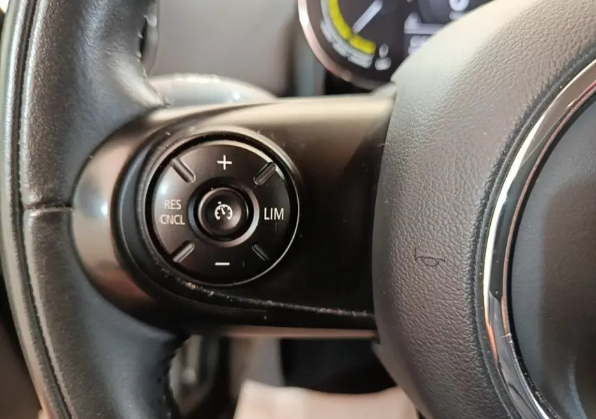 Gros plan sur le volant noir du MINI Countryman hybride, avec commandes de régulateur de vitesse au centre à gauche.