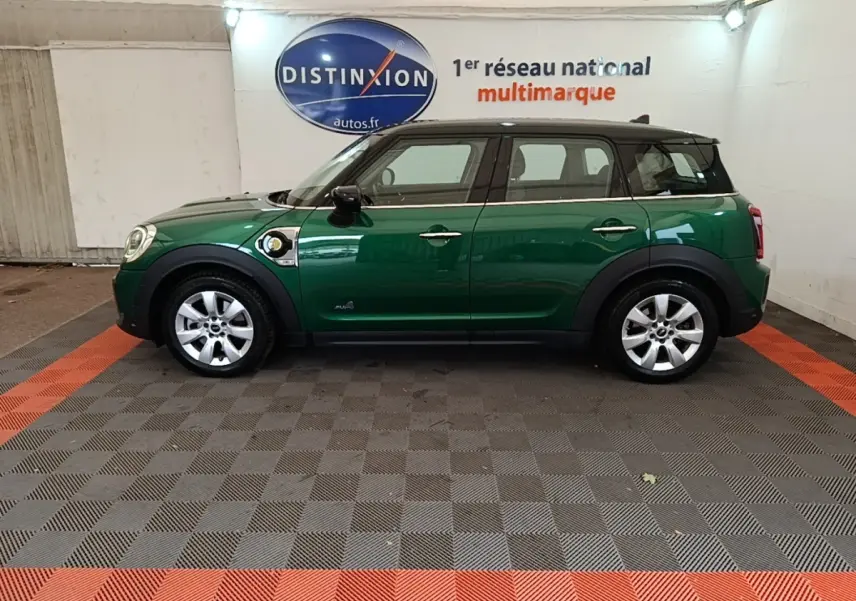 Vue de profil côté gauche d'une MINI Countryman Cooper SE hybride rechargeable vert foncé avec toit noir en intérieur showroom.
