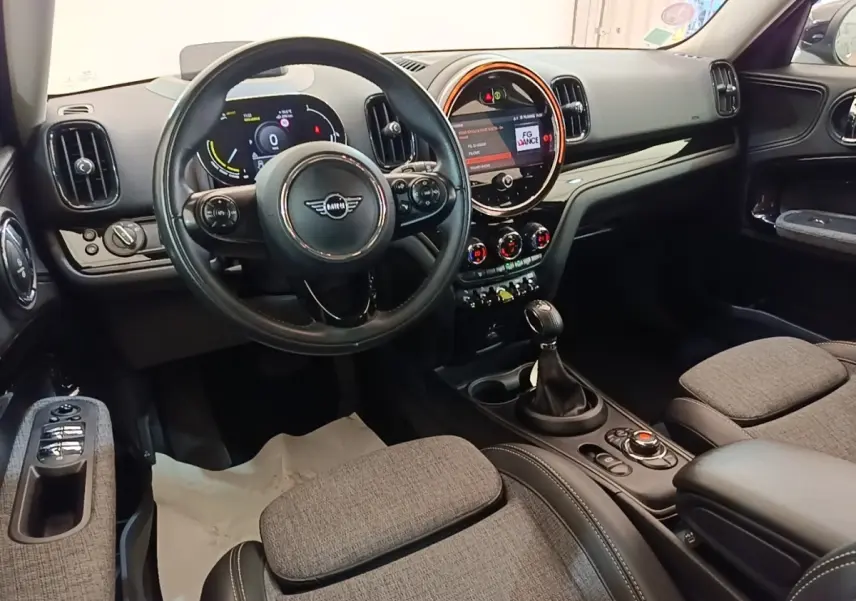 Vue intérieure avant du MINI Countryman Cooper SE avec tableau de bord numérique et sièges tissu gris clair.
