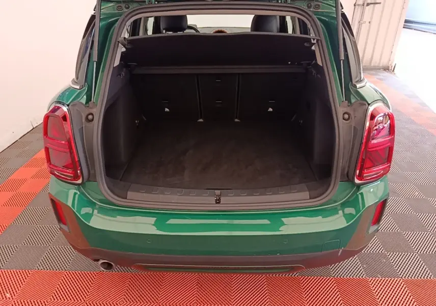 Vue arrière du coffre ouvert d'un MINI Countryman vert foncé avec tapis noir et feux arrière rouges.