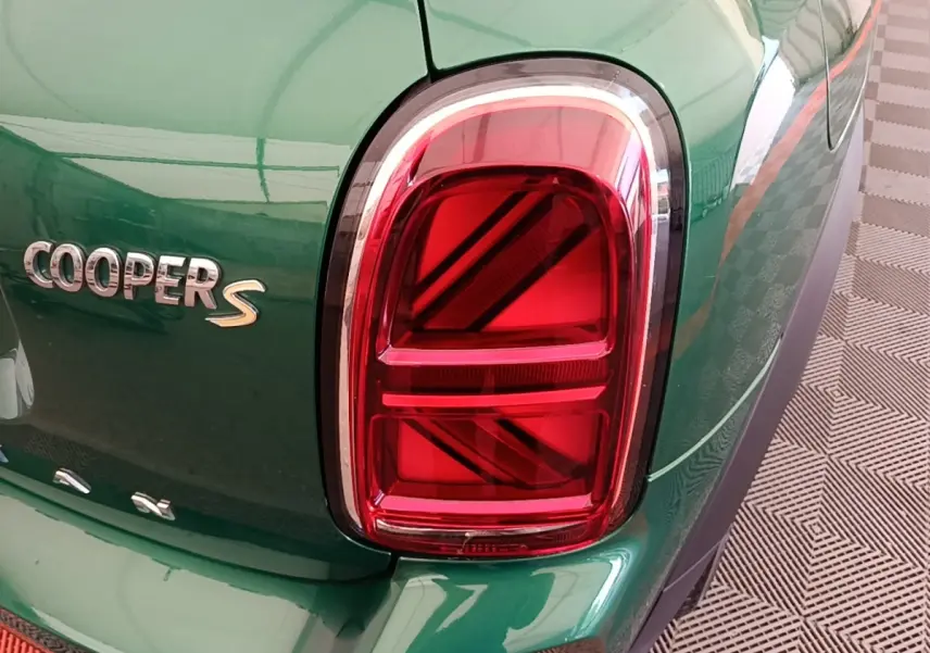 Gros plan sur le feu arrière droit rouge et le logo Cooper S d'une MINI Countryman gris clair, vue arrière partielle.