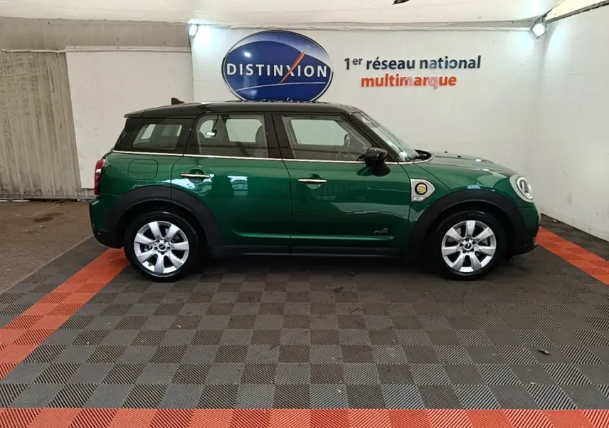Vue de profil côté gauche d'un MINI Countryman hybride rechargeable vert foncé avec toit noir en intérieur showroom.