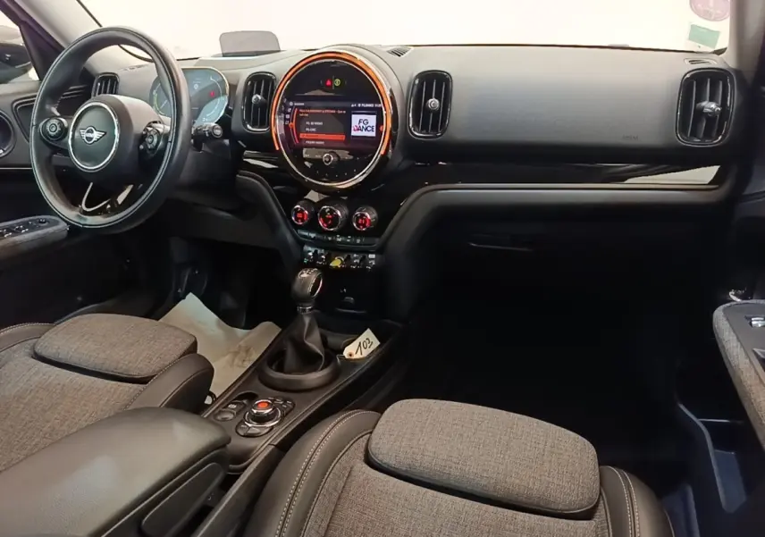 Vue intérieure avant du MINI Countryman Cooper SE, tableau de bord noir avec écran tactile rond et sièges tissu gris.