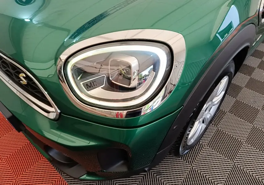 Gros plan sur le phare avant gauche et la roue d’une MINI Countryman verte, soulignant les détails chromés et le logo "S".