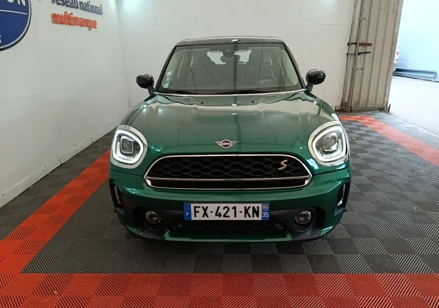 Vue avant d'une MINI Countryman Cooper SE hybride rechargeable en vert métallisé avec phares LED allumés.