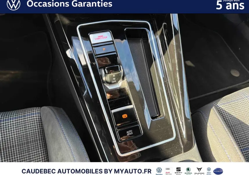 Gros plan sur la console centrale noire brillante de la Volkswagen Golf 1.5 eHybrid 2025 avec levier de vitesses et bouton de frein à main électrique.