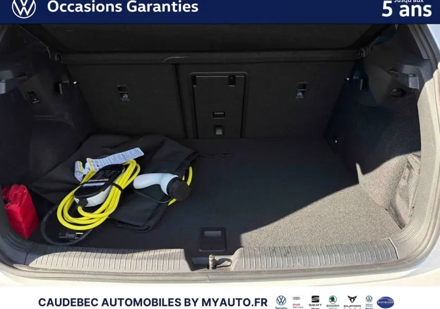 Coffre ouvert d'une Volkswagen Golf blanche 2025 avec câble de recharge électrique visible à l'intérieur.