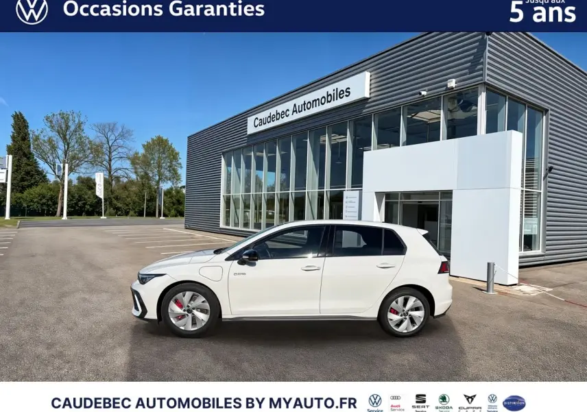 Vue latérale droite d'une Volkswagen Golf 1.5 eHybrid blanche garée devant un bâtiment moderne en verre.