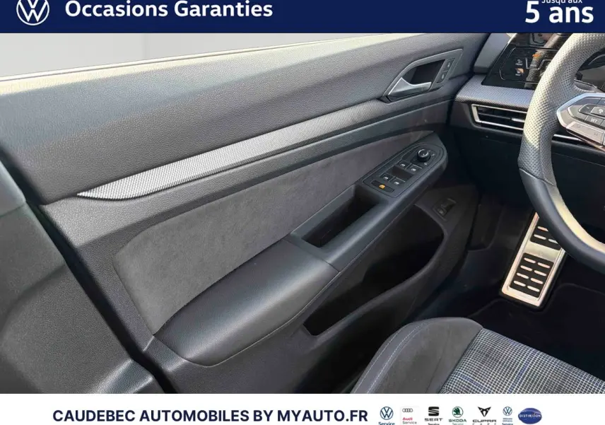 Vue intérieure côté conducteur de la porte et partie du tableau de bord d'une Volkswagen Golf 1.5 eHybrid 2025, matériaux noirs et gris.