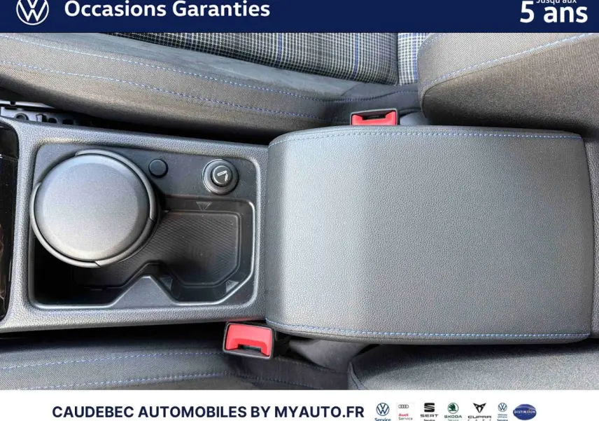 Gros plan sur l'accoudoir central noir avec surpiqûres bleues et porte-gobelets de la Volkswagen Golf blanche.