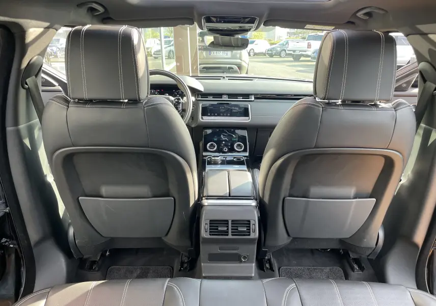Vue arrière de l'intérieur du Range Rover Velar noir Santorini 2019, sièges cuir noirs avec surpiqûres blanches et console centrale moderne.