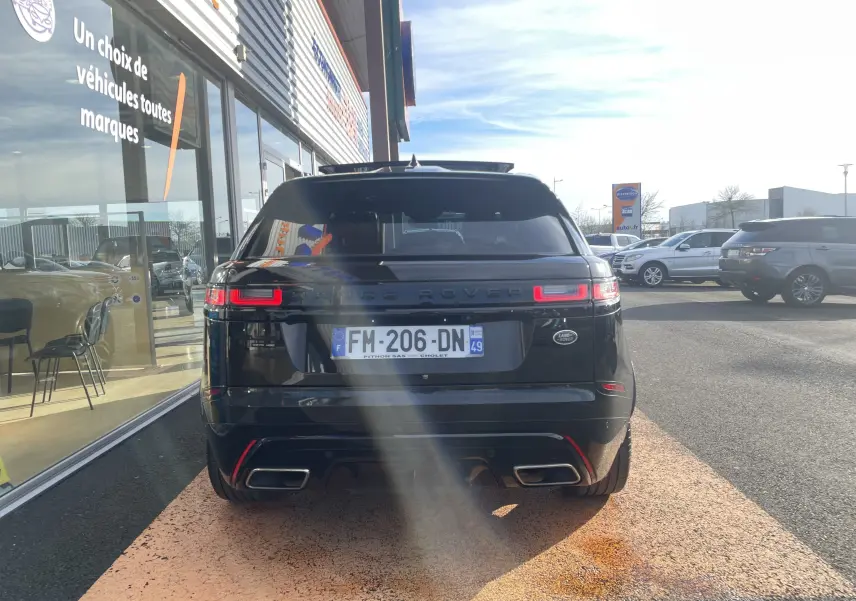 Vue arrière d'un Range Rover Velar noir Santorini garé devant un showroom, avec ses feux LED allumés.