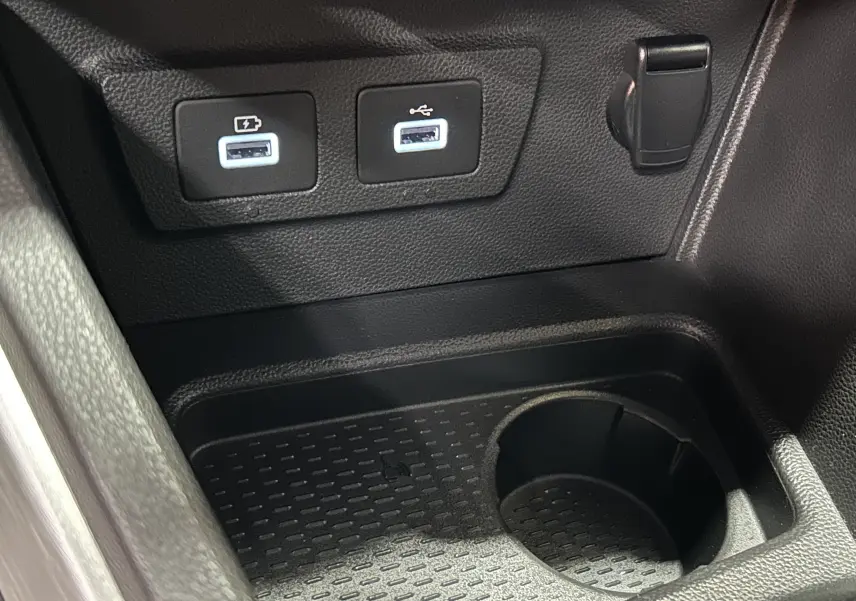 Gros plan sur la console centrale du Dacia Duster 2022 montrant deux ports USB et un porte-gobelet noir.