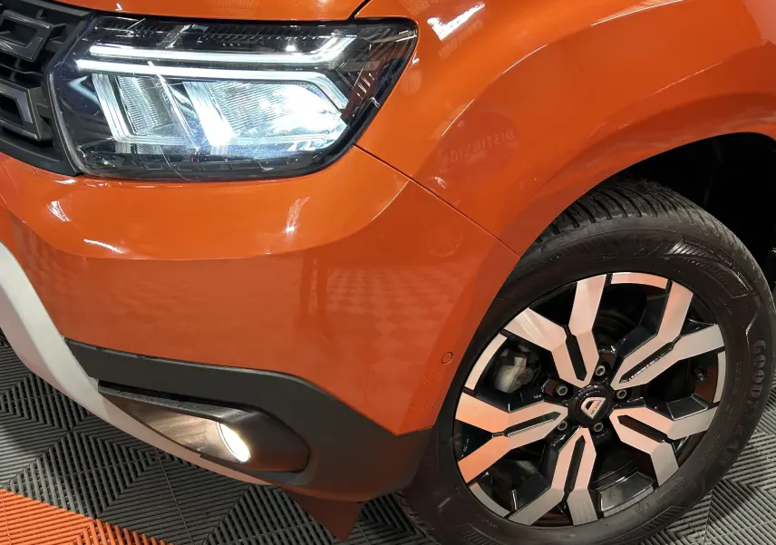 Gros plan sur l'avant droit orange Arizona du Dacia Duster 2022, mettant en valeur le phare LED et la jante alliage noire et argent.