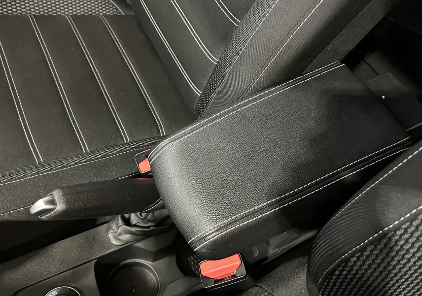 Gros plan sur l'accoudoir noir en cuir avec surpiqûres blanches entre les sièges avant en tissu noir à rayures blanches du Dacia Duster.