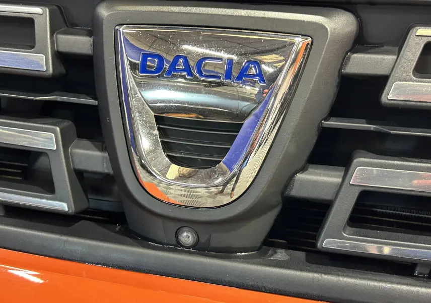 Gros plan sur la calandre orange Arizona du Dacia Duster 2022 avec logo chromé et caméra 360 intégrée en bas.