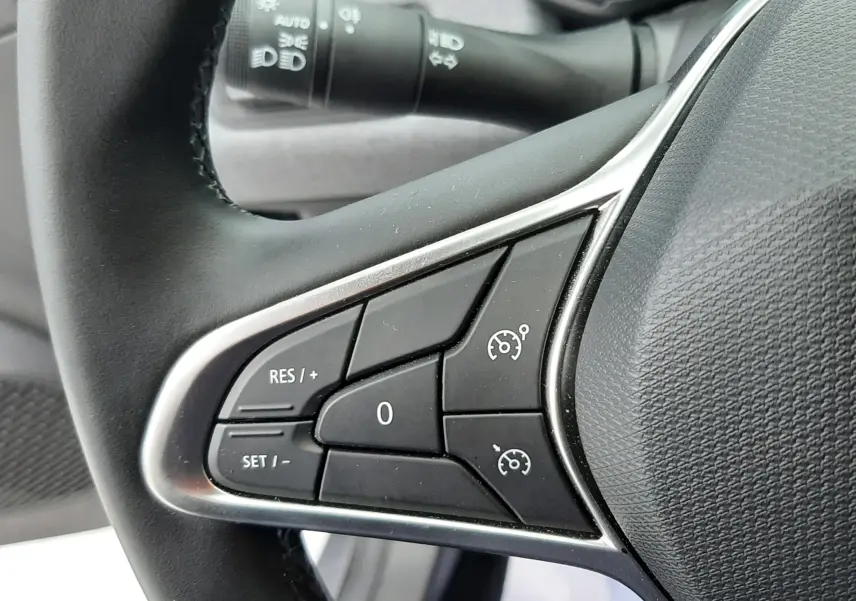 Gros plan sur les commandes de régulateur de vitesse au volant d'une Renault Clio V hybride, intérieur gris.