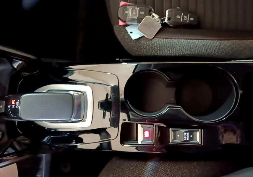 Vue plongeante sur la console centrale noire brillante de la Peugeot 208 électrique avec levier de vitesses et porte-gobelets.