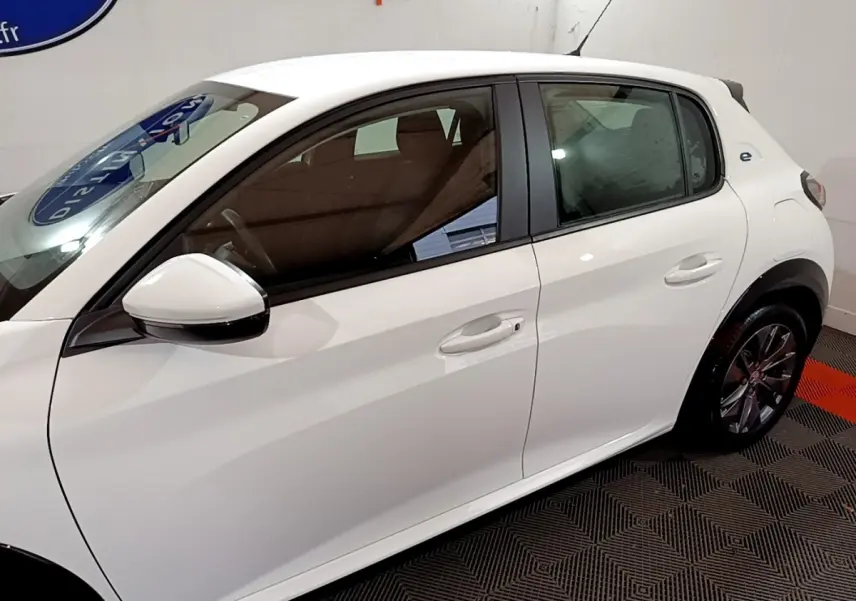 Vue côté gauche de la Peugeot 208 Electrique Active Business blanche, avec rétroviseur et poignées de porte visibles.