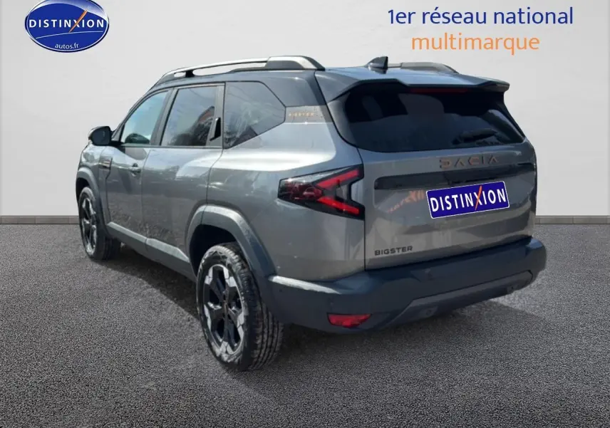 Vue 3/4 arrière droit du Dacia Bigster gris schiste avec barres de toit et jantes alliage noires.
