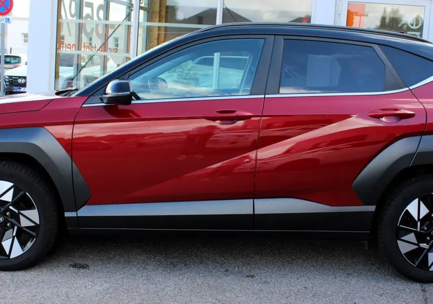 Vue latérale gauche du Hyundai Kona 2024 rouge Ultimate Metal avec toit noir et jantes bicolores distinctives.