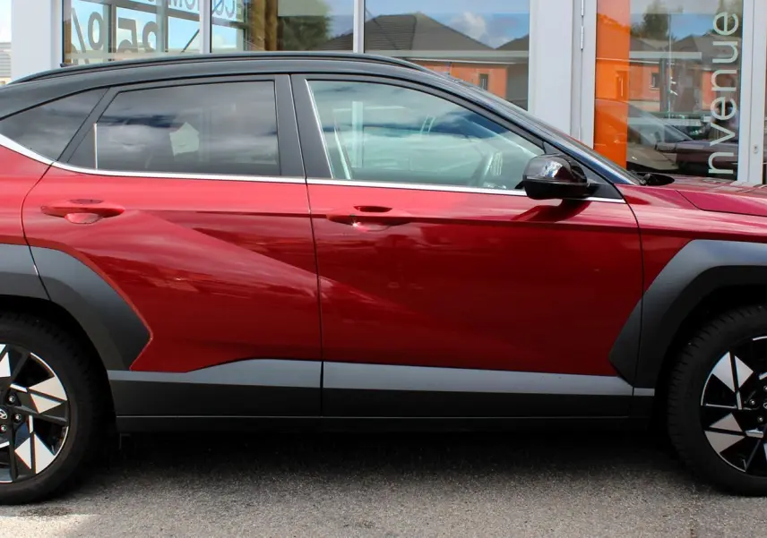 Vue de profil côté gauche du Hyundai Kona 2024 rouge Ultimate Metal avec toit noir et jantes bicolores distinctives.