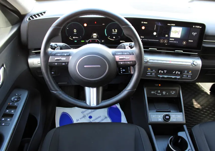 Vue intérieure centrée sur le volant cuir noir et le tableau de bord numérique du Hyundai Kona hybride 2024.