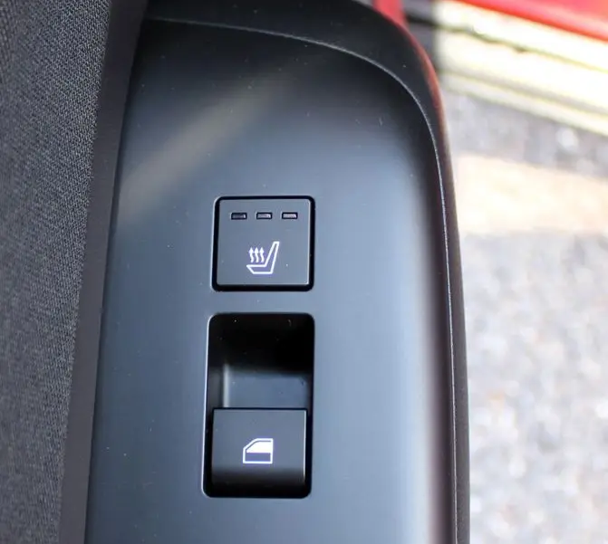 Gros plan sur les commandes de siège chauffant et de lève-vitre côté conducteur du Hyundai Kona rouge 2024.