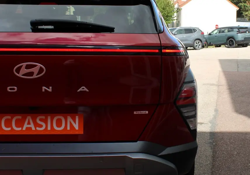 Vue arrière d'un Hyundai Kona rouge Ultimate Metal avec bande lumineuse LED et logo hybride visible sur un parking.