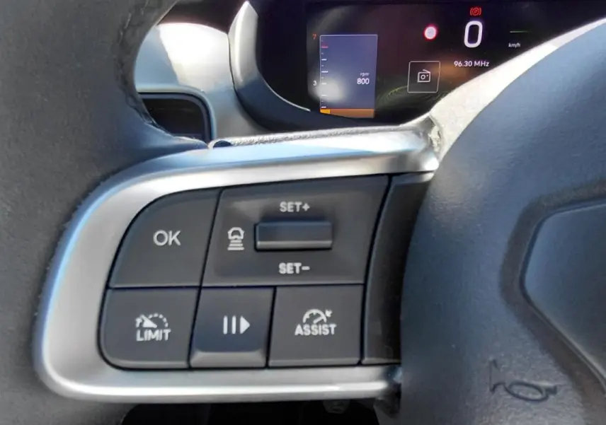 Gros plan sur les commandes à gauche du volant du Jeep Avenger blanc 2025, avec affichage numérique en arrière-plan.