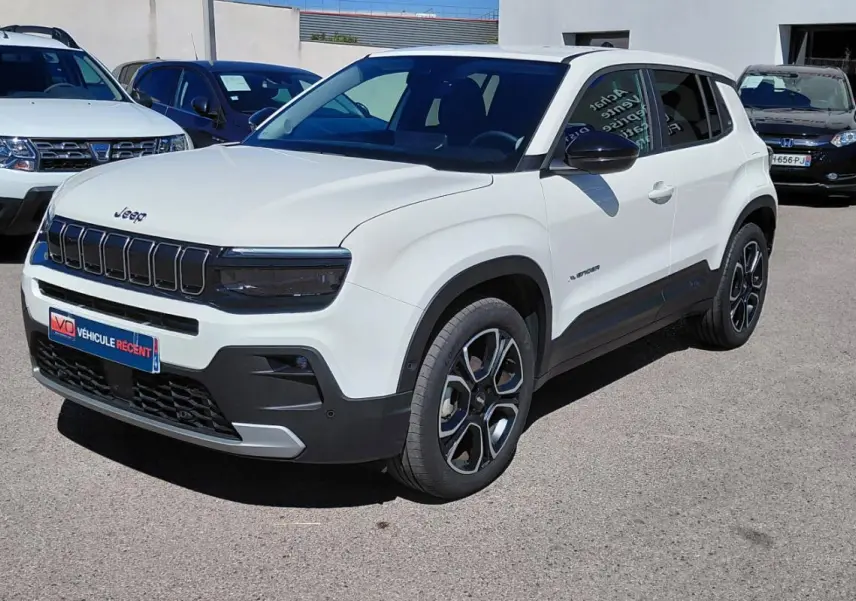Jeep Avenger blanc en 3/4 avant droit, avec calandre noire et jantes distinctives, stationné en extérieur.