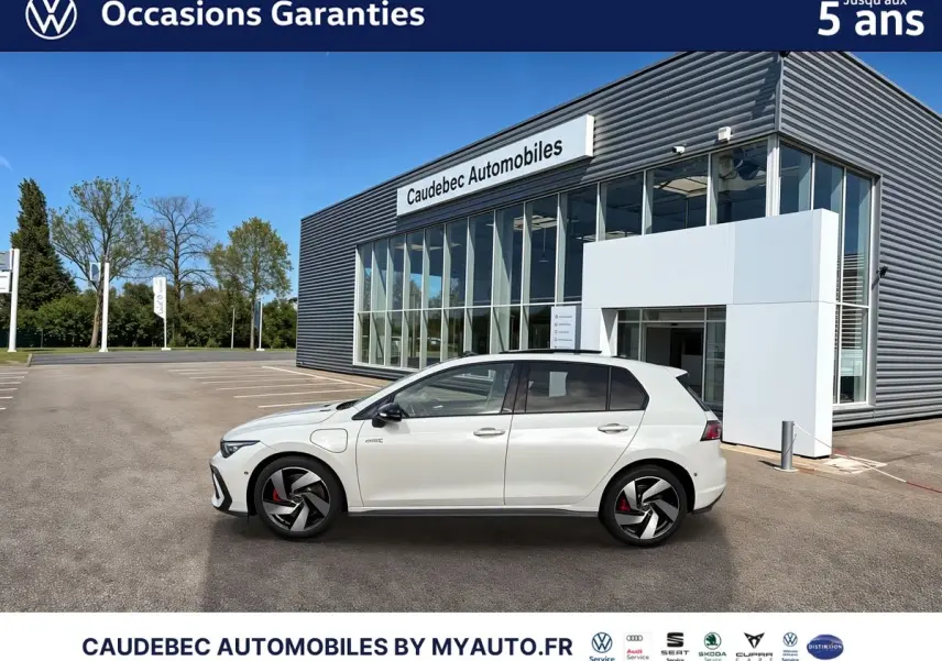 Vue de profil côté gauche d'une Volkswagen Golf 1.5 eHybrid blanche stationnée devant un bâtiment moderne en verre.