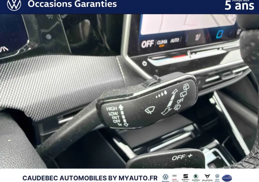 Gros plan sur la commande des essuie-glaces dans l'habitacle d'une Volkswagen Golf blanche, avec écran tactile en arrière-plan.