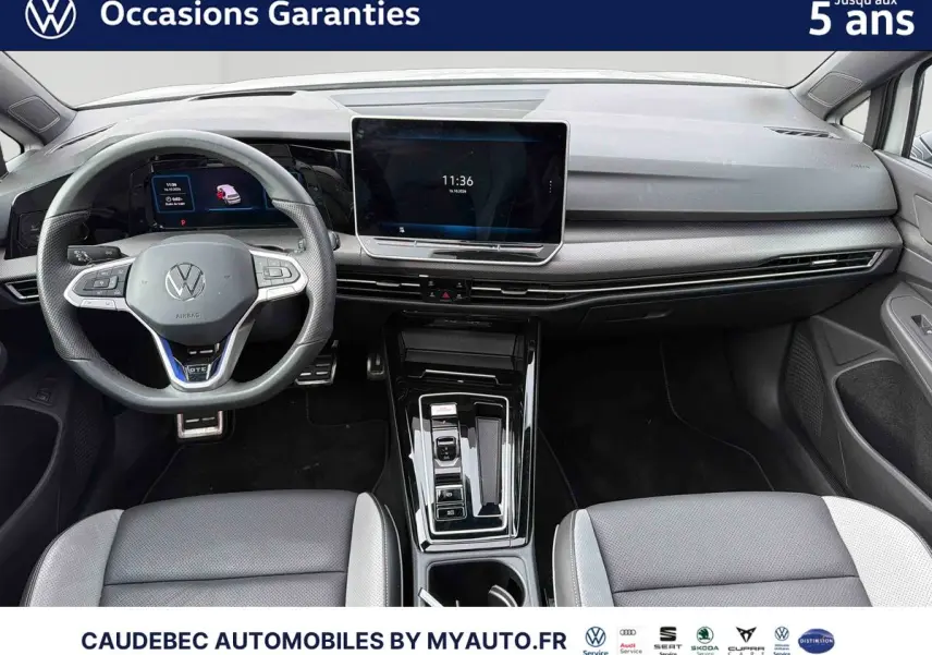 Vue intérieure avant de la Volkswagen Golf 1.5 eHybrid 272 DSG6 blanche, tableau de bord moderne avec écran tactile central et volant sport cuir.