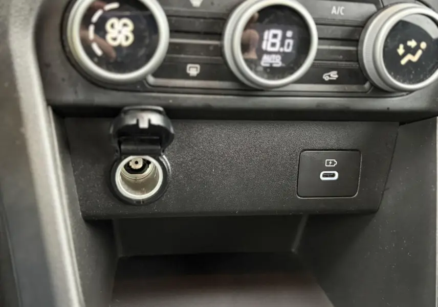 Gros plan sur la console centrale du Dacia Jogger 2025, montrant la prise allume-cigare et un port USB-C de recharge.