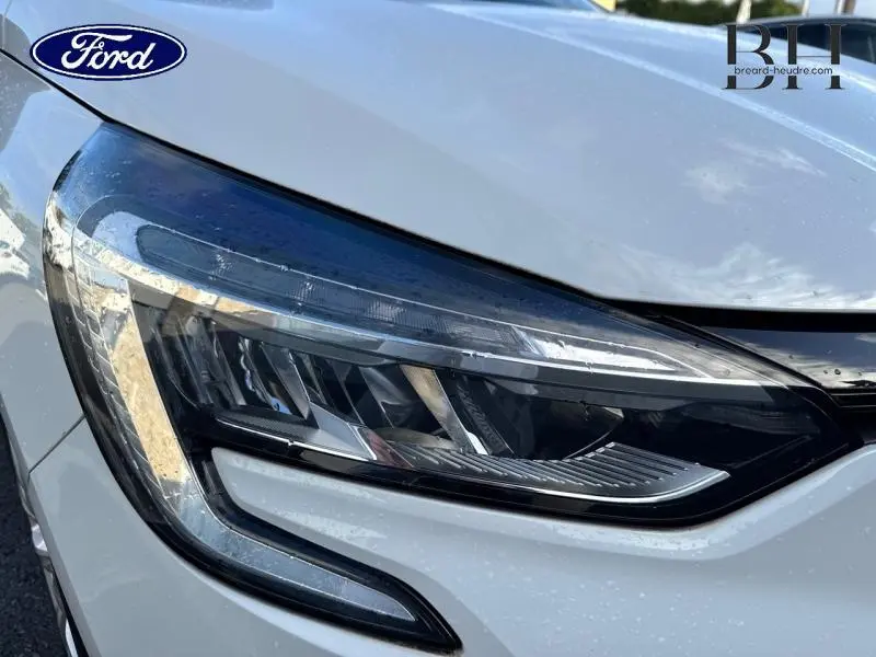 Gros plan sur le phare avant droit blanc de la Renault Clio 1.0 SCe 65ch Life 2020 avec détails LED et carrosserie brillante.