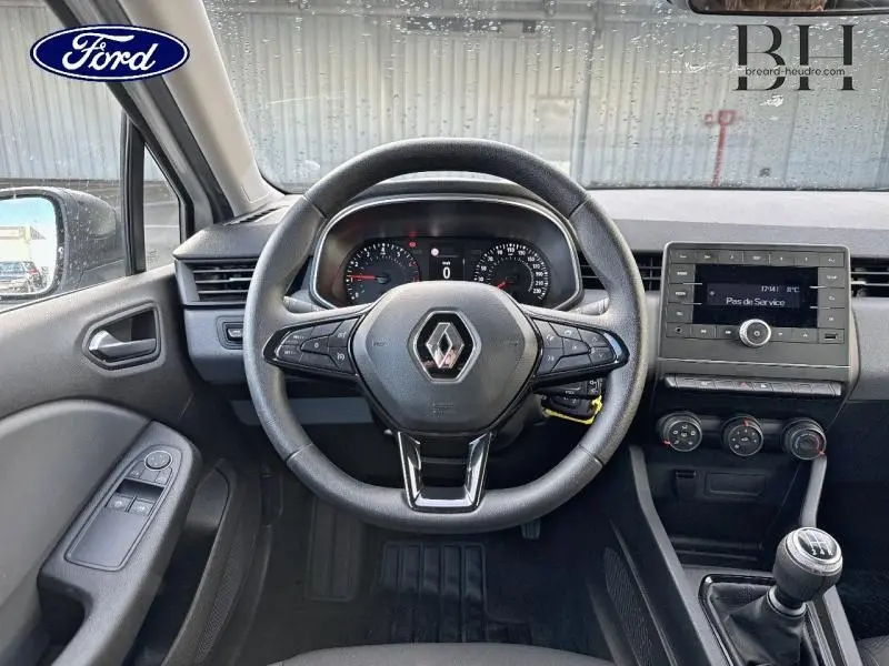 Vue intérieure centrée sur le volant noir de la Renault Clio blanche, tableau de bord et console avec boîte manuelle visibles.