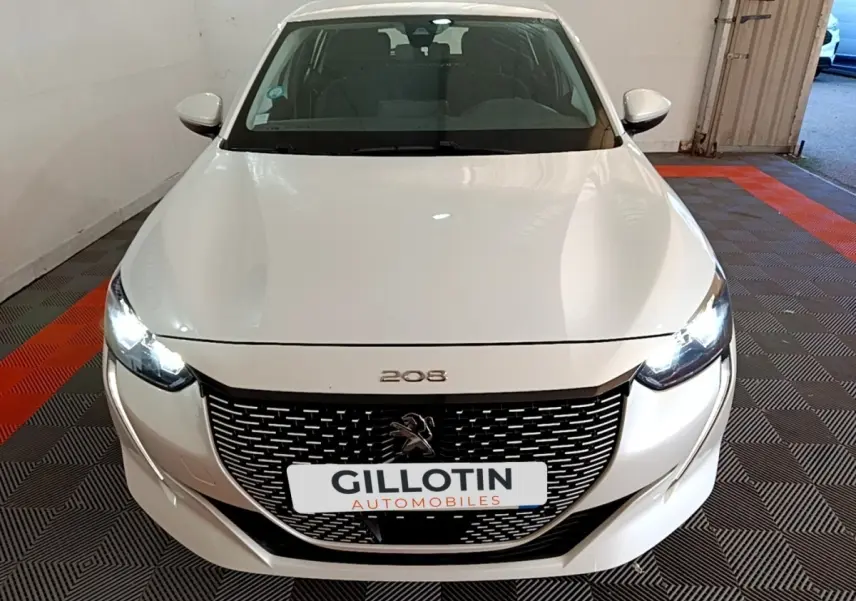 Vue avant d'une Peugeot 208 électrique Active Business blanche avec phares LED allumés en intérieur.