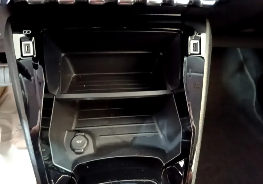 Vue rapprochée de la console centrale noire du Peugeot 208 électrique avec prise 12V et ports USB visibles.
